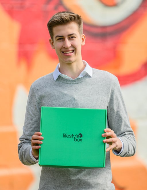 Moritz Lechner mit der Lifestylebox in den Händen vor einem orangen Hintergrund.